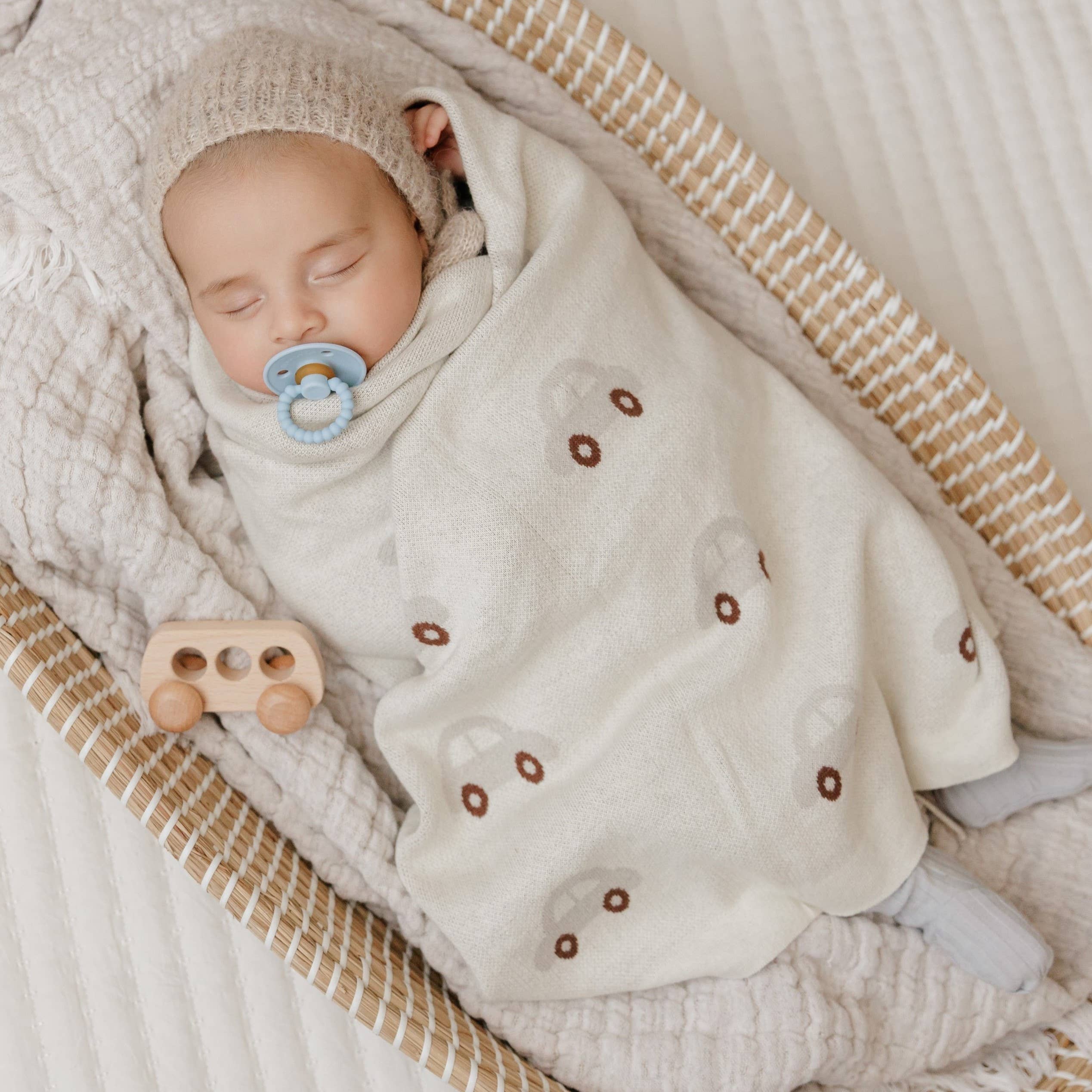 Newborn baby wrapped in a soft blanket with a pacifier and wooden toy in a crib.