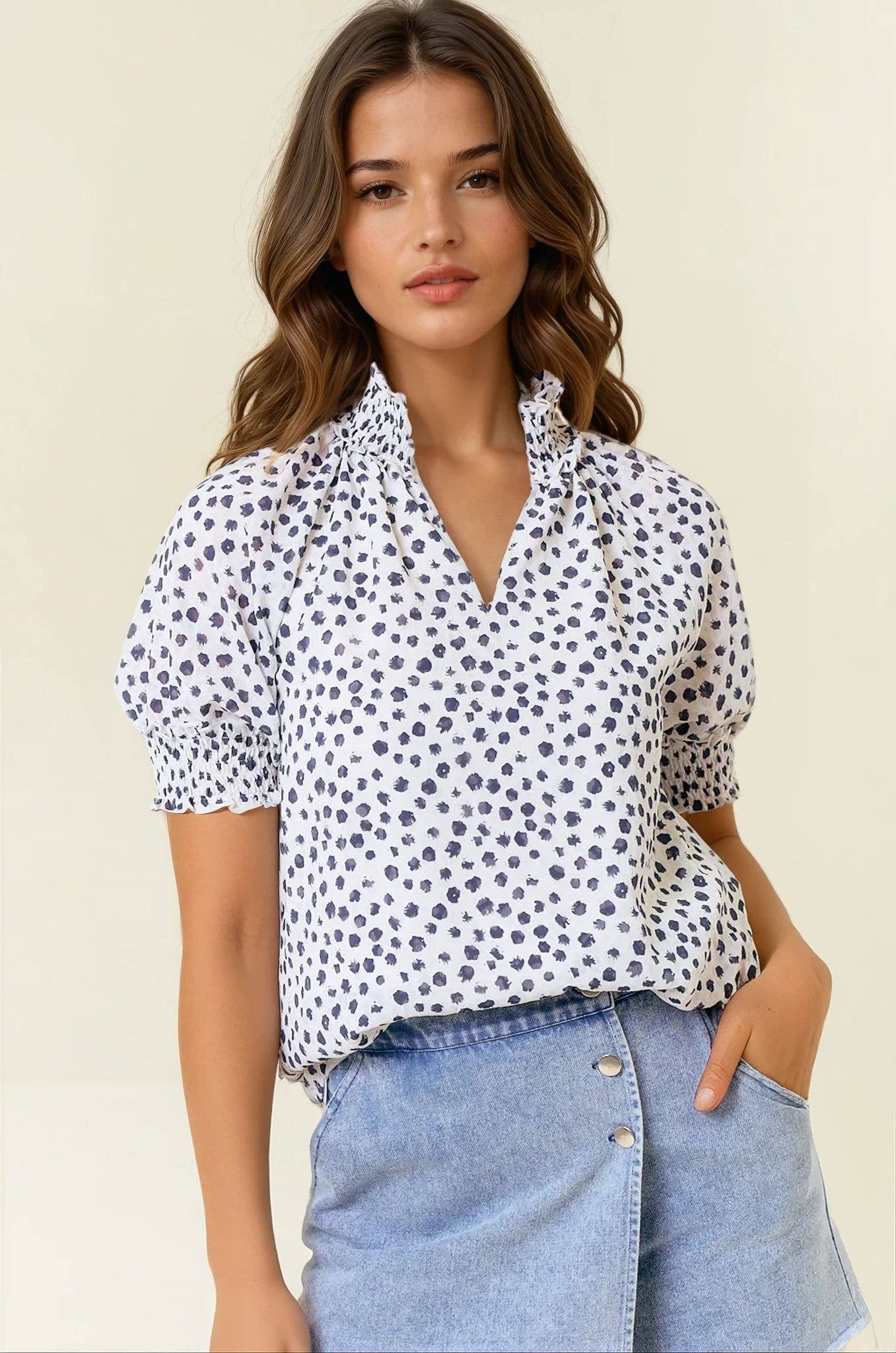 Woman wearing a white blouse with black polka dots and blue jeans on a beige background