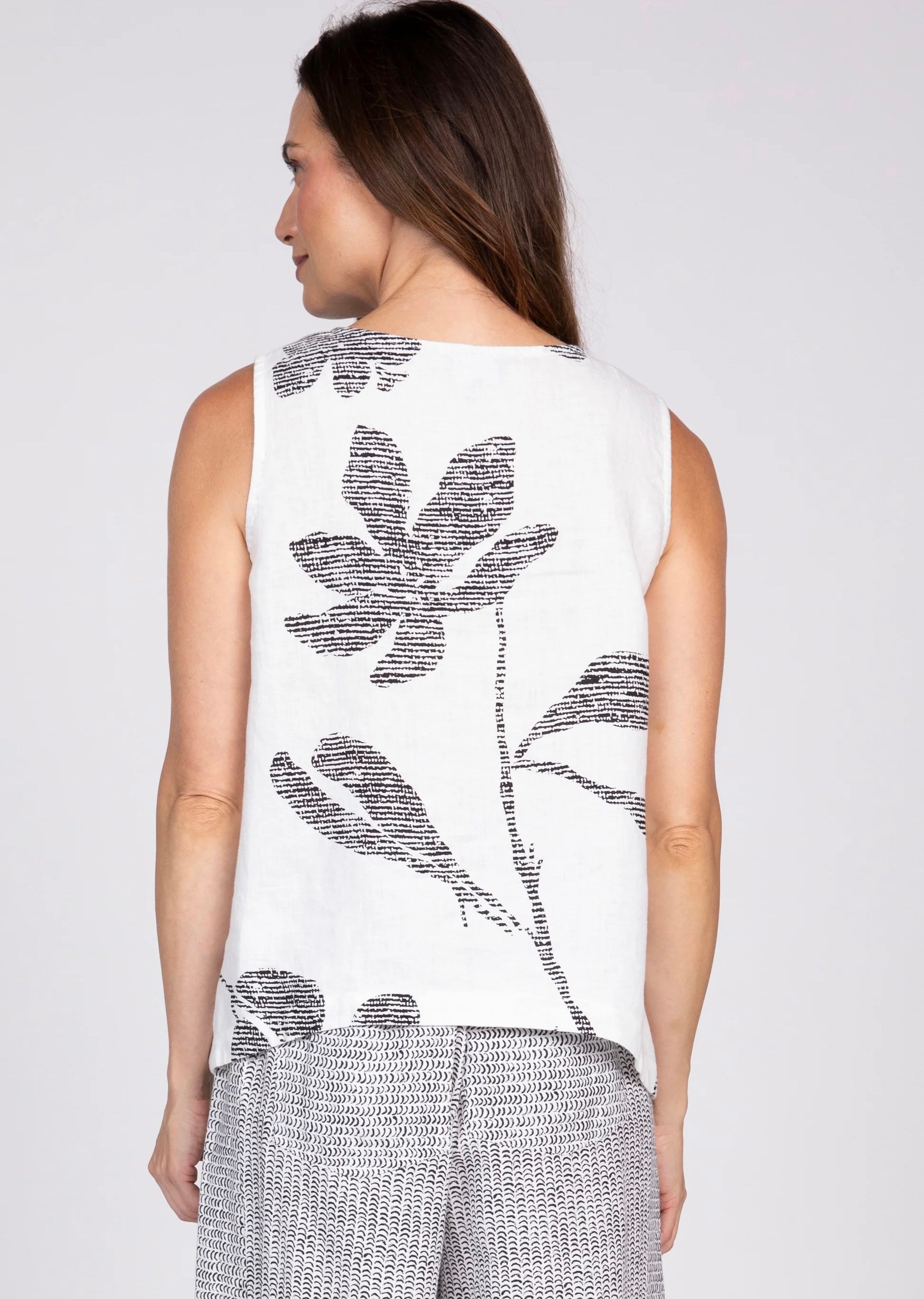 IMG_0133 — Women's white sleeveless tank top with black oversized floral bouquet print, front view, scoop neckline
IMG_0136 — Olivia women's white floral bouquet tank top, front torso view showing bold black botanical print
IMG_0135 — Women's white floral print tank top styled with black and white wide-leg pants and black platform sandals, full body front view
IMG_0134 — Women's white sleeveless tank top with large black leaf and floral print, back view
IMG_0137 — Close-up back view of women's white tank to