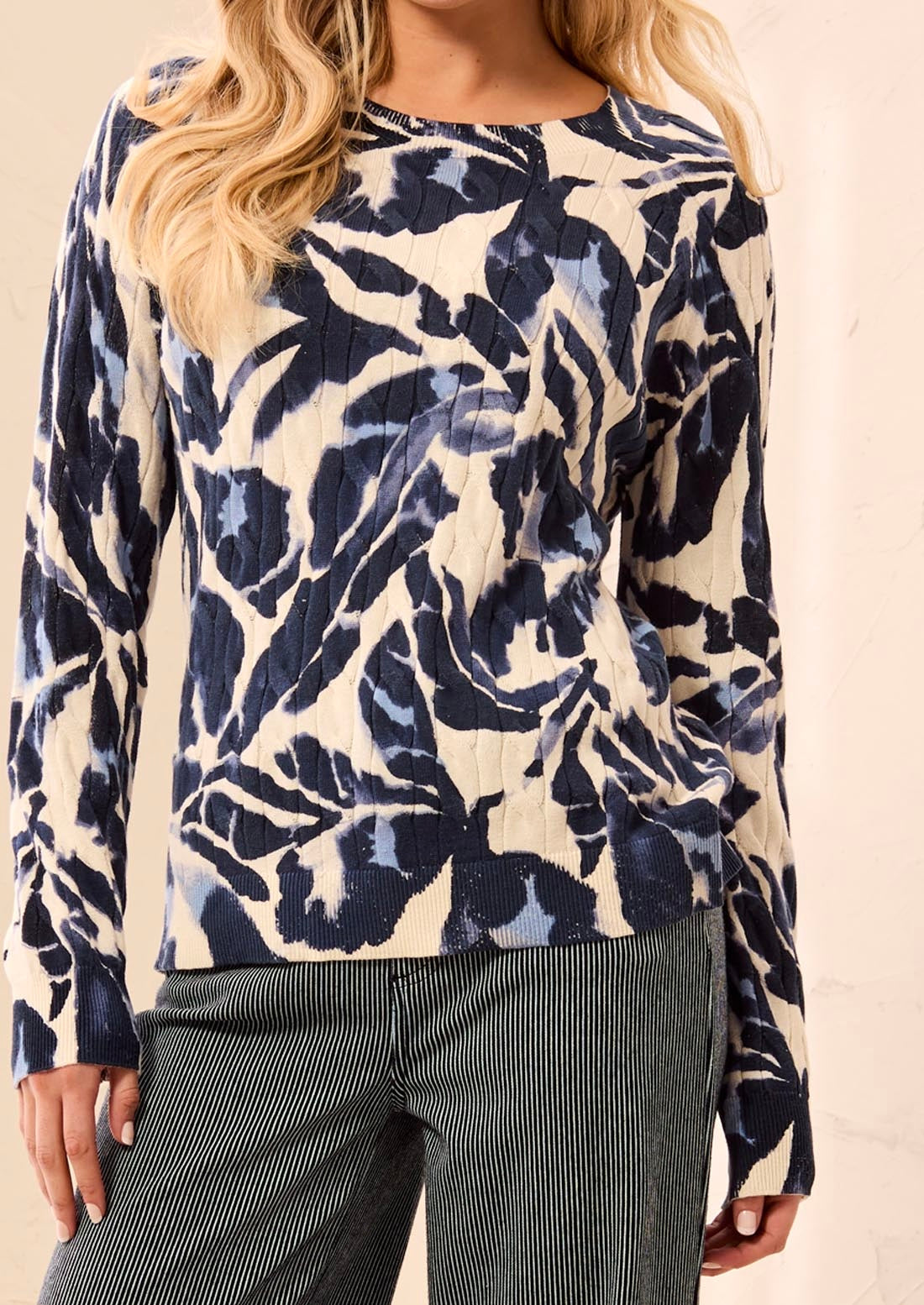 A woman wearing a long-sleeve top with a navy blue and beige abstract floral pattern, paired with dark gray pinstriped pants.