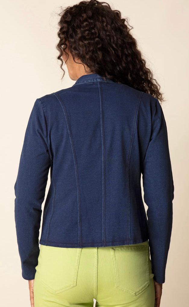 A woman viewed from the back wearing a dark navy blue cropped jacket and lime green pants, set against a plain beige background.