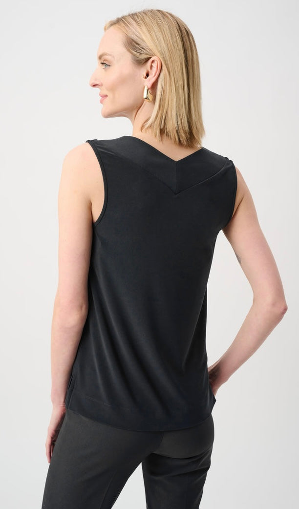 A woman shown from the back wearing a black sleeveless top with a V-neckline and dark pants, photographed against a light gray studio background.