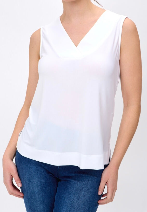 A woman wearing a white sleeveless V-neck top and blue jeans, shown from the neck down against a light gray studio background.