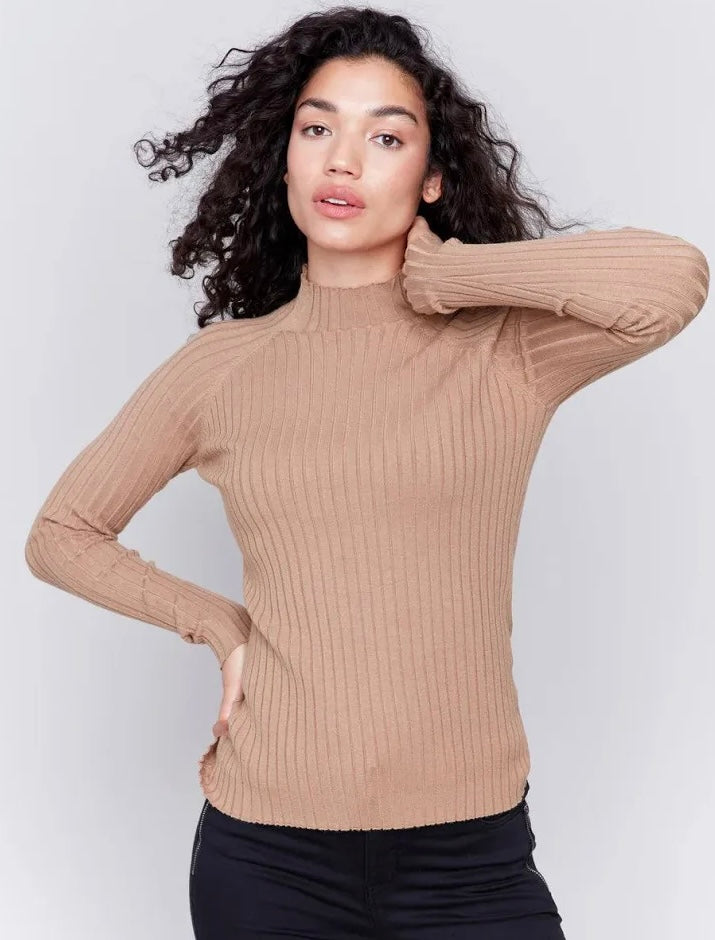 A woman modeling a beige ribbed mock neck long-sleeve sweater against a light gray studio background.