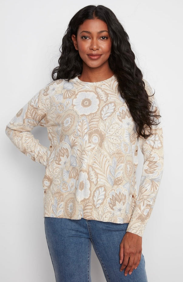 A woman modeling a beige and white floral patterned long-sleeve knit top with blue jeans, standing against a plain white studio background.