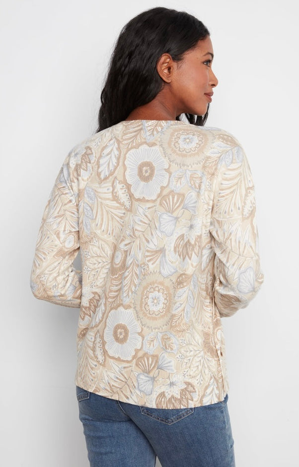 A woman shown from the back wearing a beige long-sleeve top with a cream and light blue floral pattern, paired with blue jeans, against a plain white background.