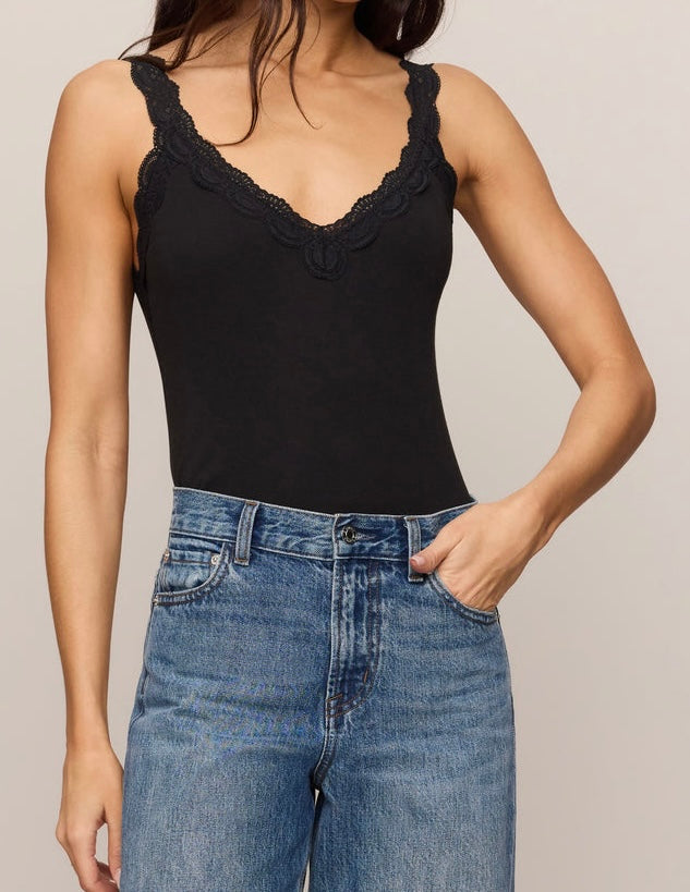 A woman wearing a black lace-trimmed camisole top and blue jeans, shown from the neck down against a plain light gray studio background.
