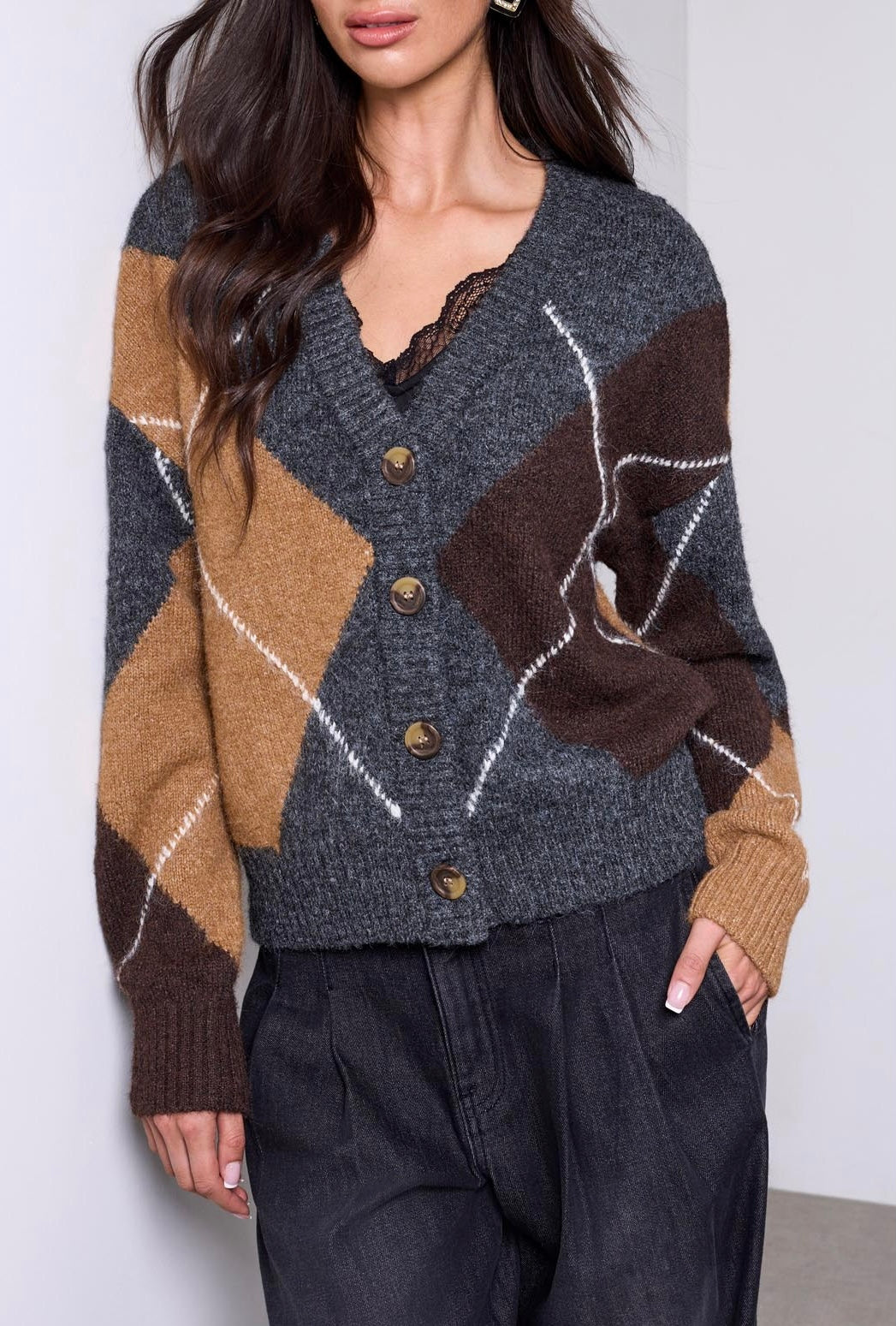 A woman wearing a gray, brown, and tan argyle cardigan sweater with wooden buttons, paired with dark gray pants.