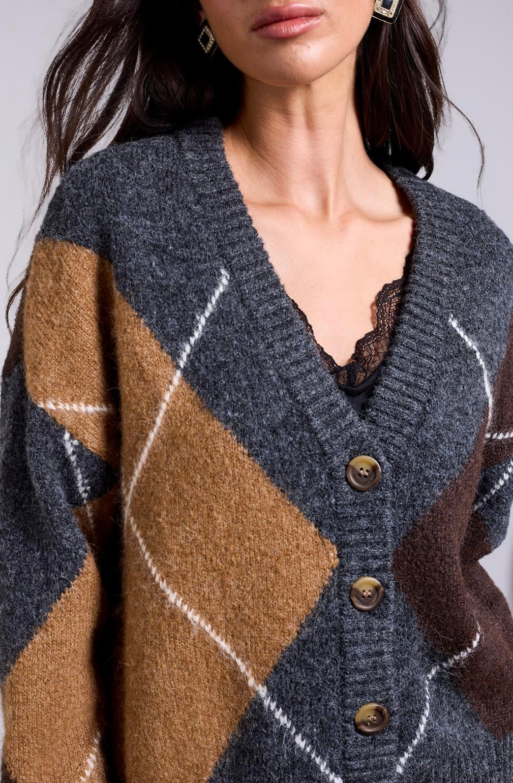 Close-up of a woman wearing a fuzzy knit cardigan with an argyle pattern in charcoal gray, tan, brown, and white, featuring three brown buttons.