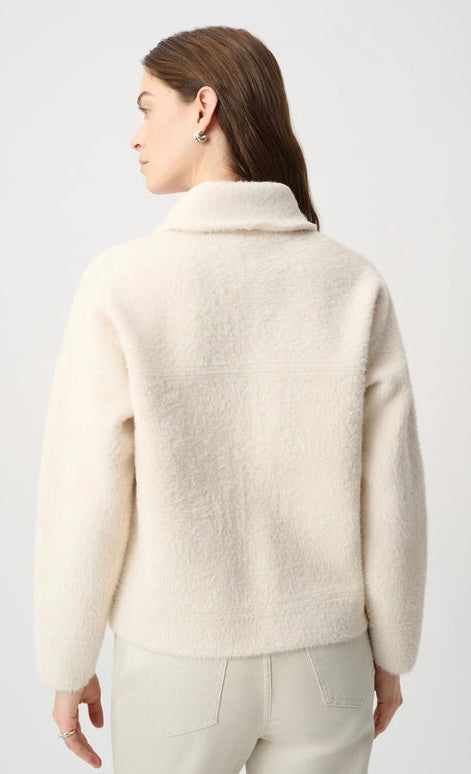 A woman shown from the back wearing a cream-colored, textured bouclé fleece jacket and matching light trousers against a plain light gray studio background.
