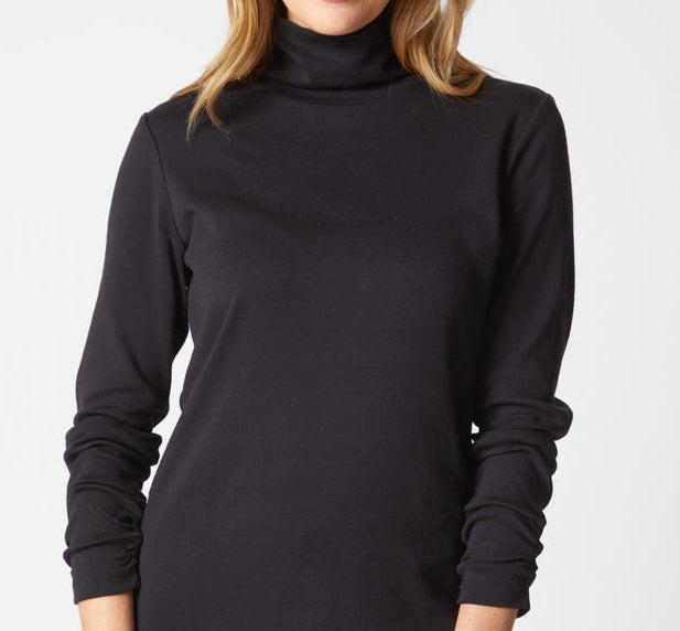 A woman wearing a black long-sleeve turtleneck top, shown from the neck down against a plain light gray background.