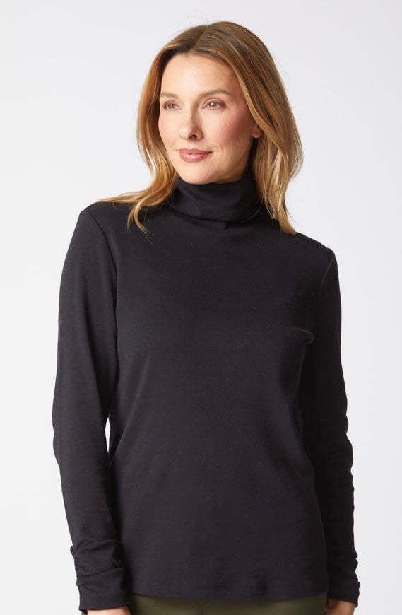 A woman wearing a black long-sleeve turtleneck top, photographed against a clean light gray studio background.