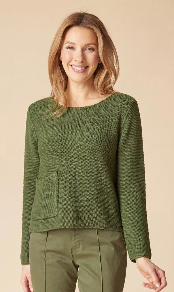 A woman wearing a textured olive green knit sweater with a side pocket and matching olive green pants, standing against a solid beige background.