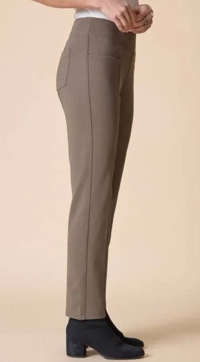 A person shown from the waist down wearing slim taupe-brown trousers and black ankle boots against a plain beige studio background.