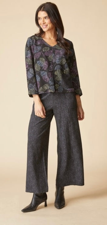 A woman modeling a dark floral long-sleeve blouse with wide-leg charcoal gray pants and black ankle boots, standing against a plain beige studio background.
