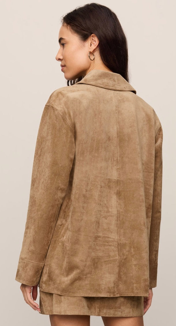 A woman shown from the back wearing a tan suede or faux-suede blazer and matching mini skirt against a plain light beige studio background. -OLIVIA'S
