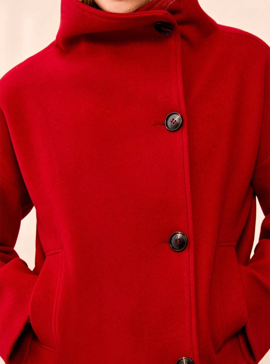 A close-up of a bright red coat with a high stand collar and three dark buttons, worn by a model. - OLIVIA'S