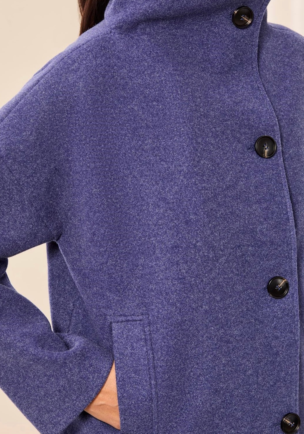 Close-up of a person wearing a textured heathered blue-purple coat with black buttons and a high collar, with a hand in a pocket. - OLIVIA'S