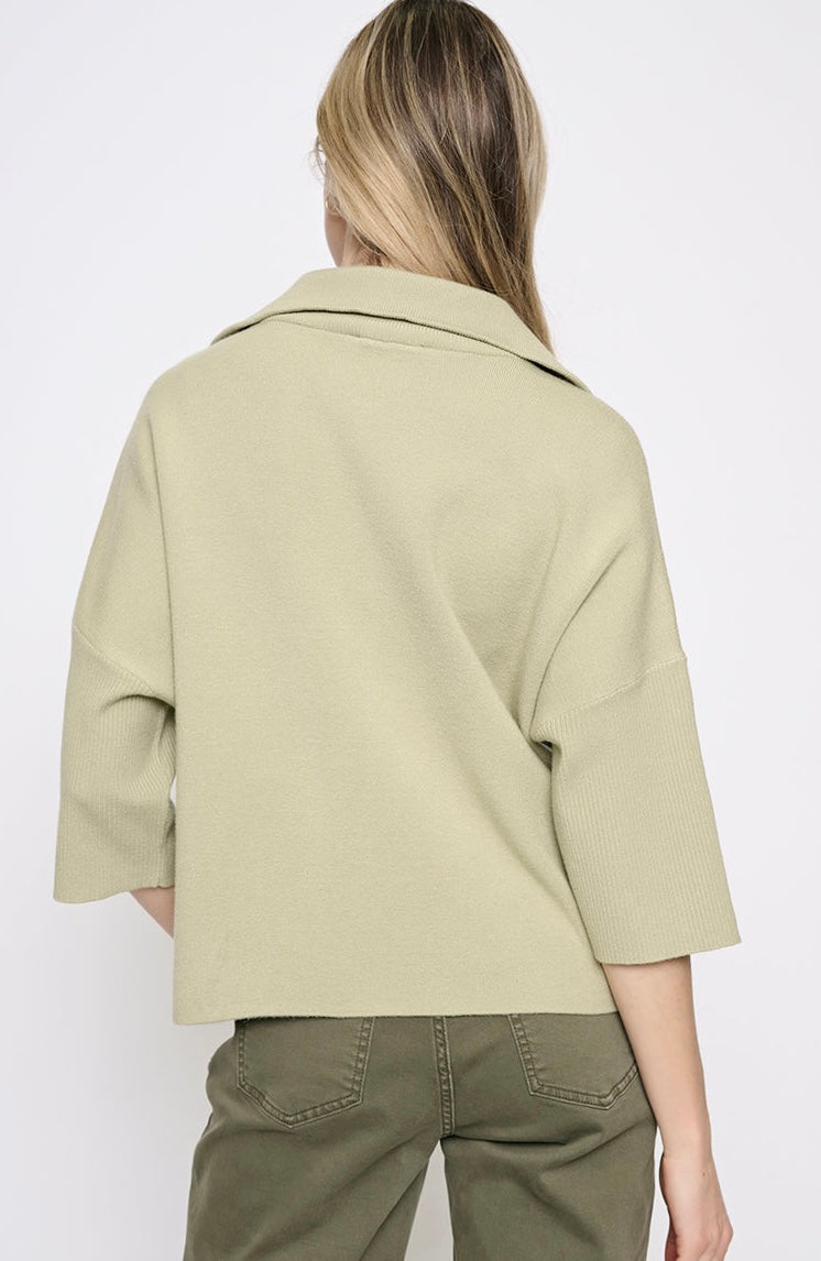 A woman shown from the back wearing a light sage green knit top with three-quarter sleeves and olive green pants, against a plain white background. -OLIVIA'S