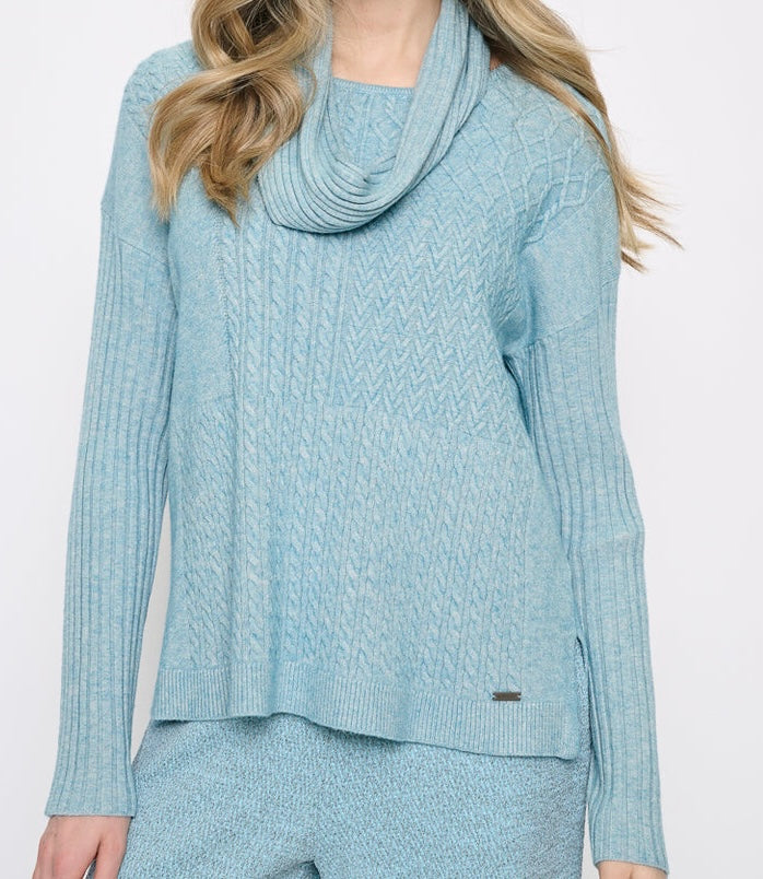 A woman wearing a light blue cable-knit sweater with a draped cowl neck and matching knit pants, shown against a plain white studio background. - OLIVIA'S