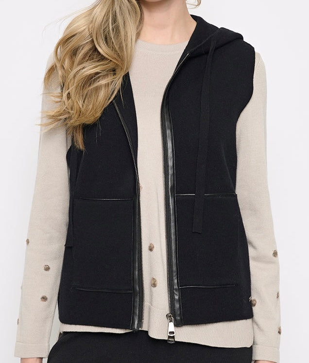 A woman wearing a black sleeveless zip-front hooded vest over a beige long-sleeve top with decorative buttons on the sleeves, shown against a plain light background. - OLIVIA'S