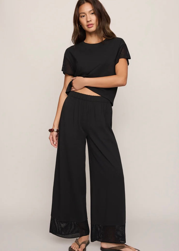 Woman wearing a black outfit with wide-leg pants on a plain background