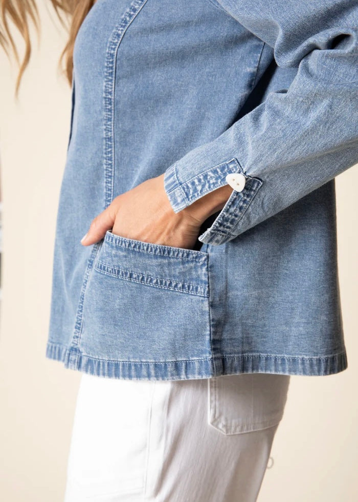 Close-up of a person wearing a light blue denim jacket with rolled-up sleeves on a beige background