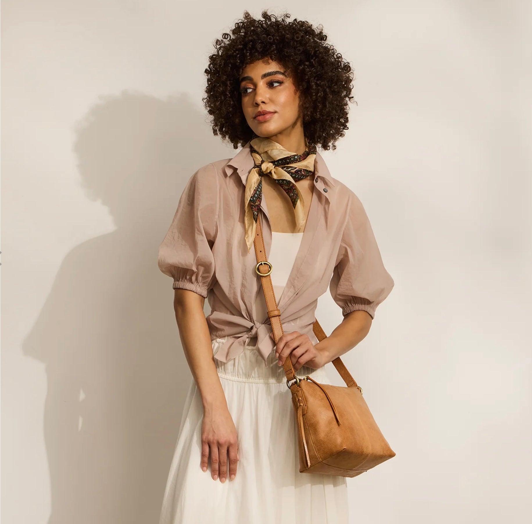 Woman holding a brown leather handbag against a plain background