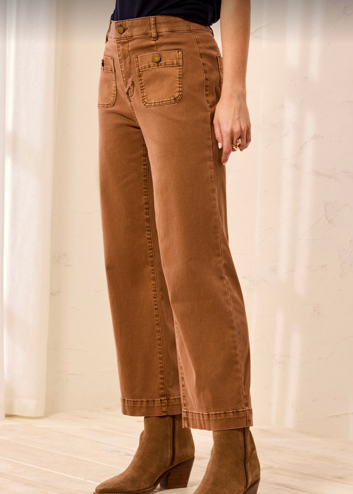 A person wearing brown wide-leg cropped jeans with a dark top and brown ankle boots, shown from the waist down in a softly lit indoor setting.