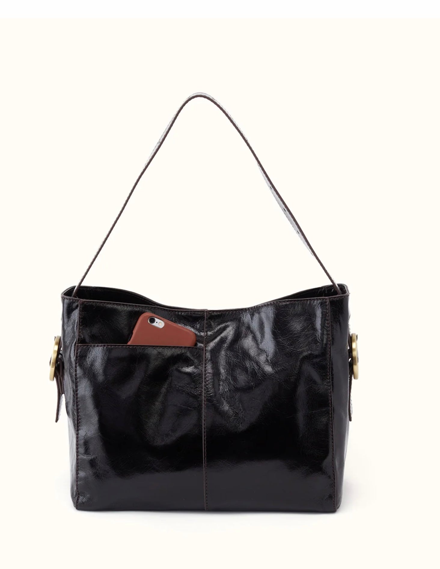 A black patent leather shoulder bag with a single strap, side gold-tone hardware, and a brown leather accent tab on the front pocket, shown against a plain off-white background.