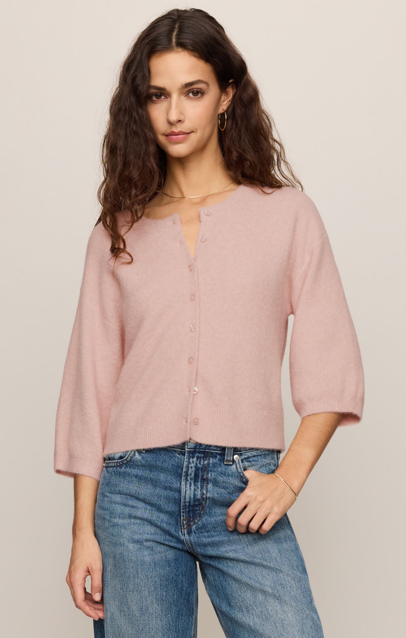 Woman wearing a light pink blouse and blue jeans against a plain background