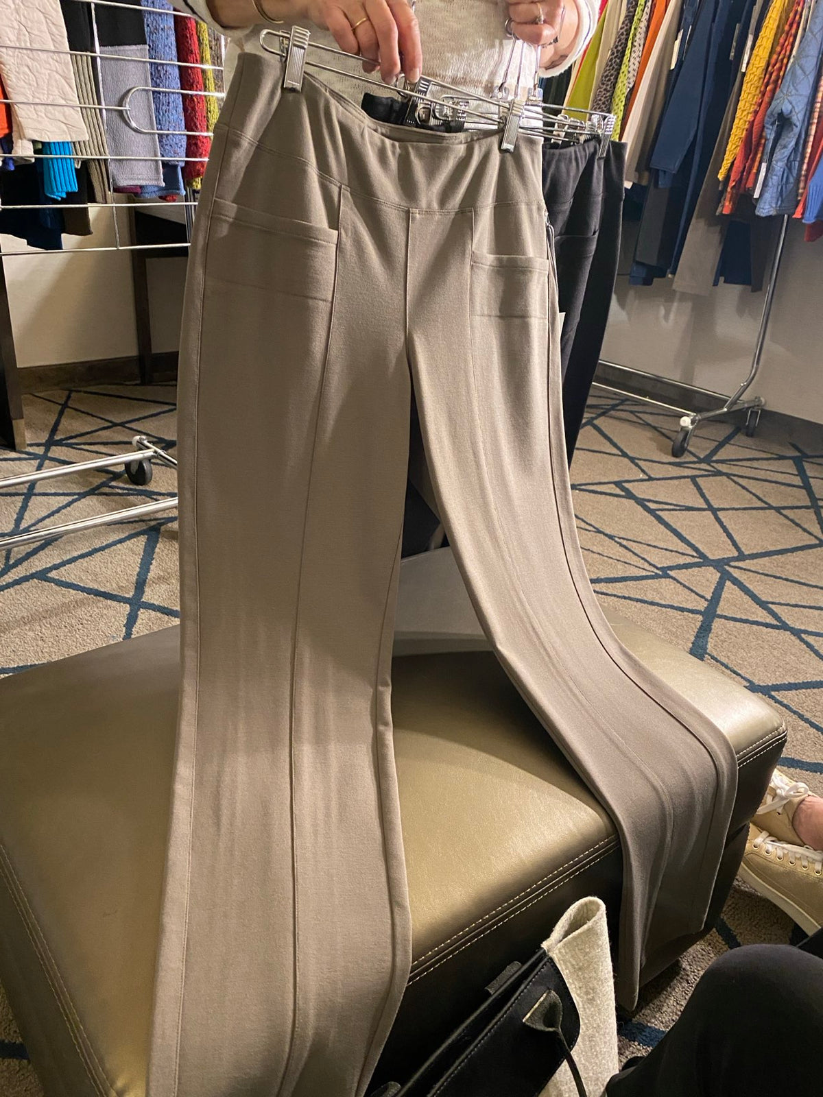 A pair of beige wide-leg pants hanging on a clear plastic hanger, displayed on a beige leather chair in a retail store setting.