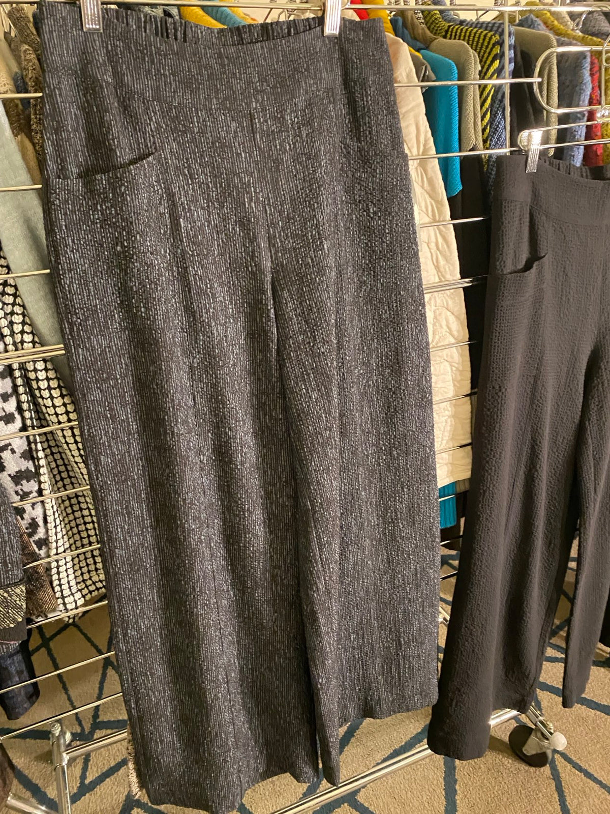 A dark gray heathered knit sweater or long-sleeve top laid flat on a metal rack, with other folded garments visible in the background.