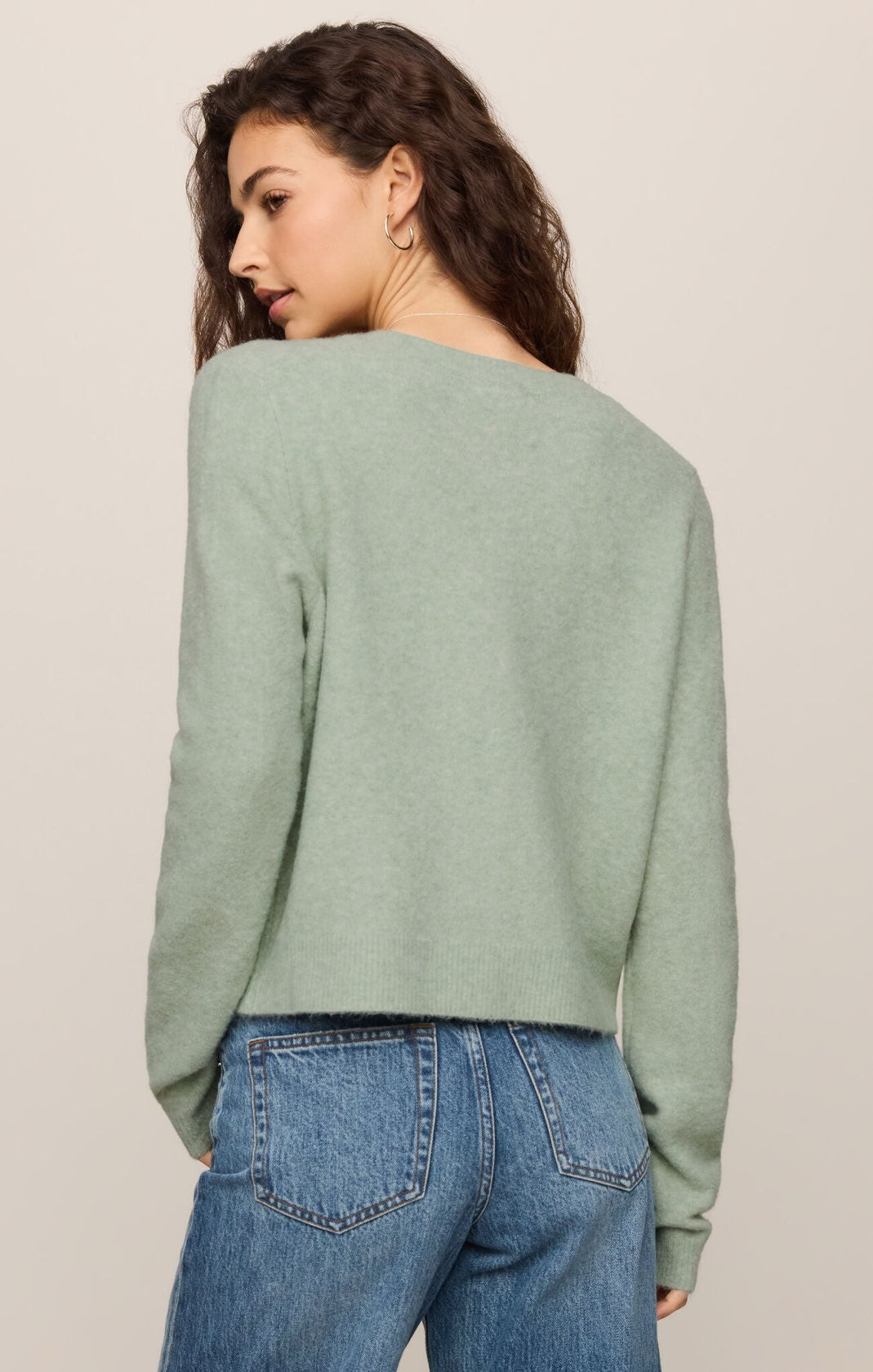 Woman wearing a light green sweater and blue jeans on a beige background