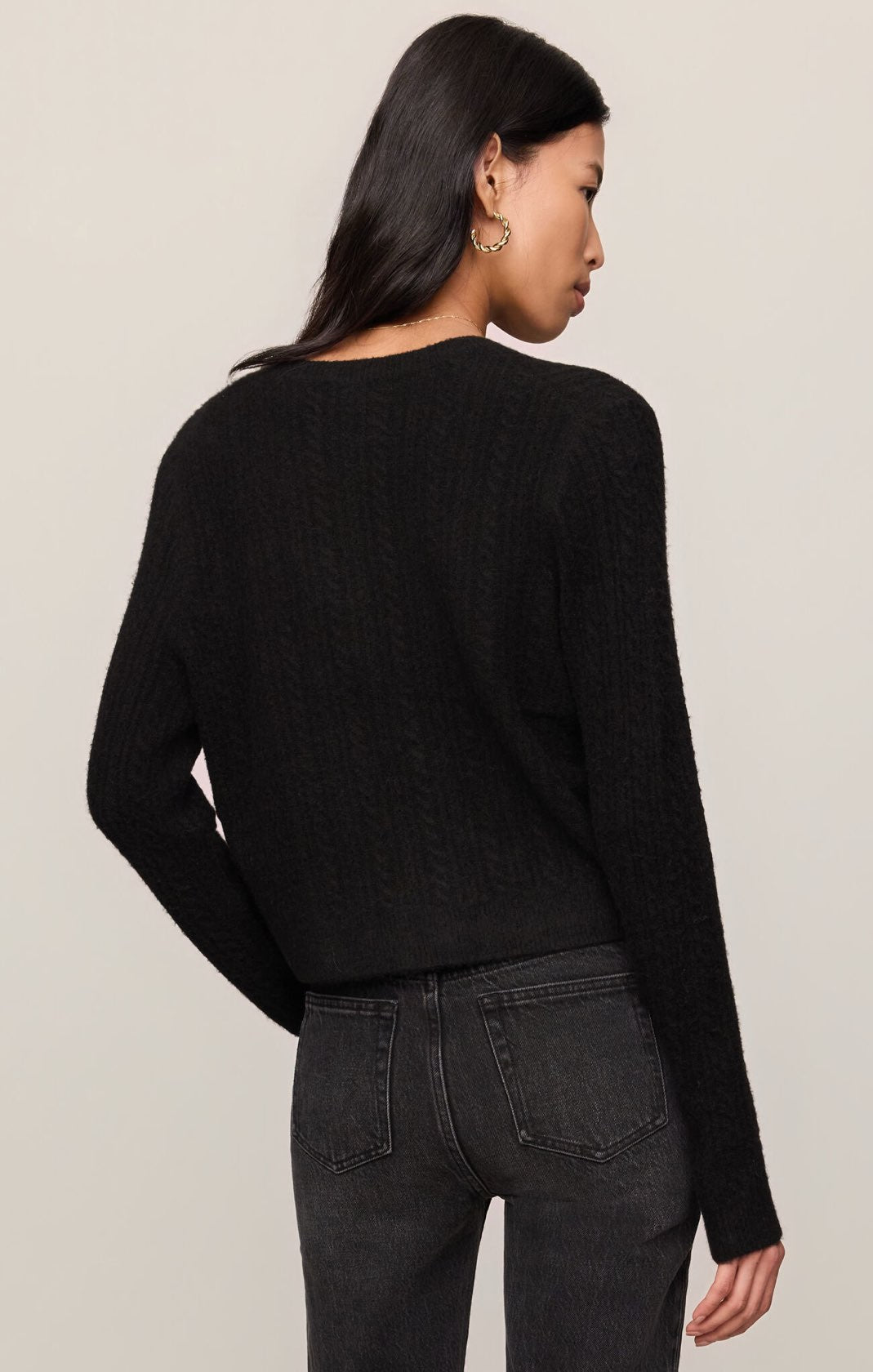 Person wearing a black sweater and dark jeans against a plain background