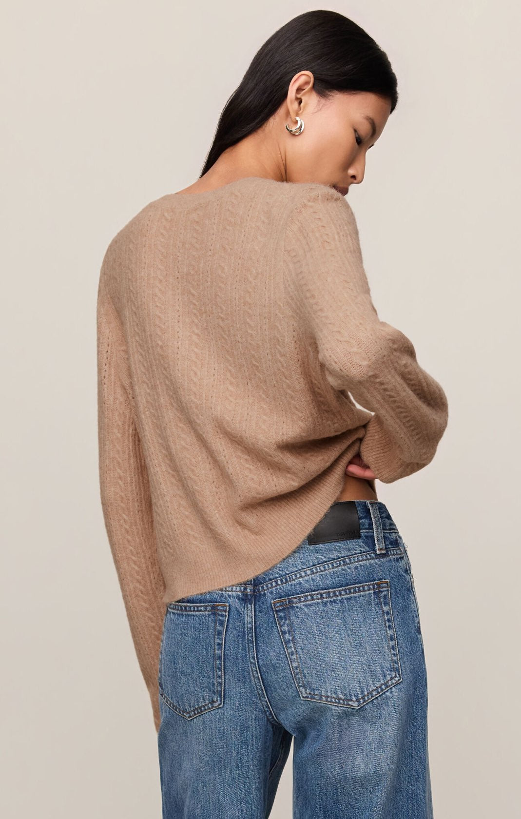 Person wearing a beige sweater and blue jeans against a plain background