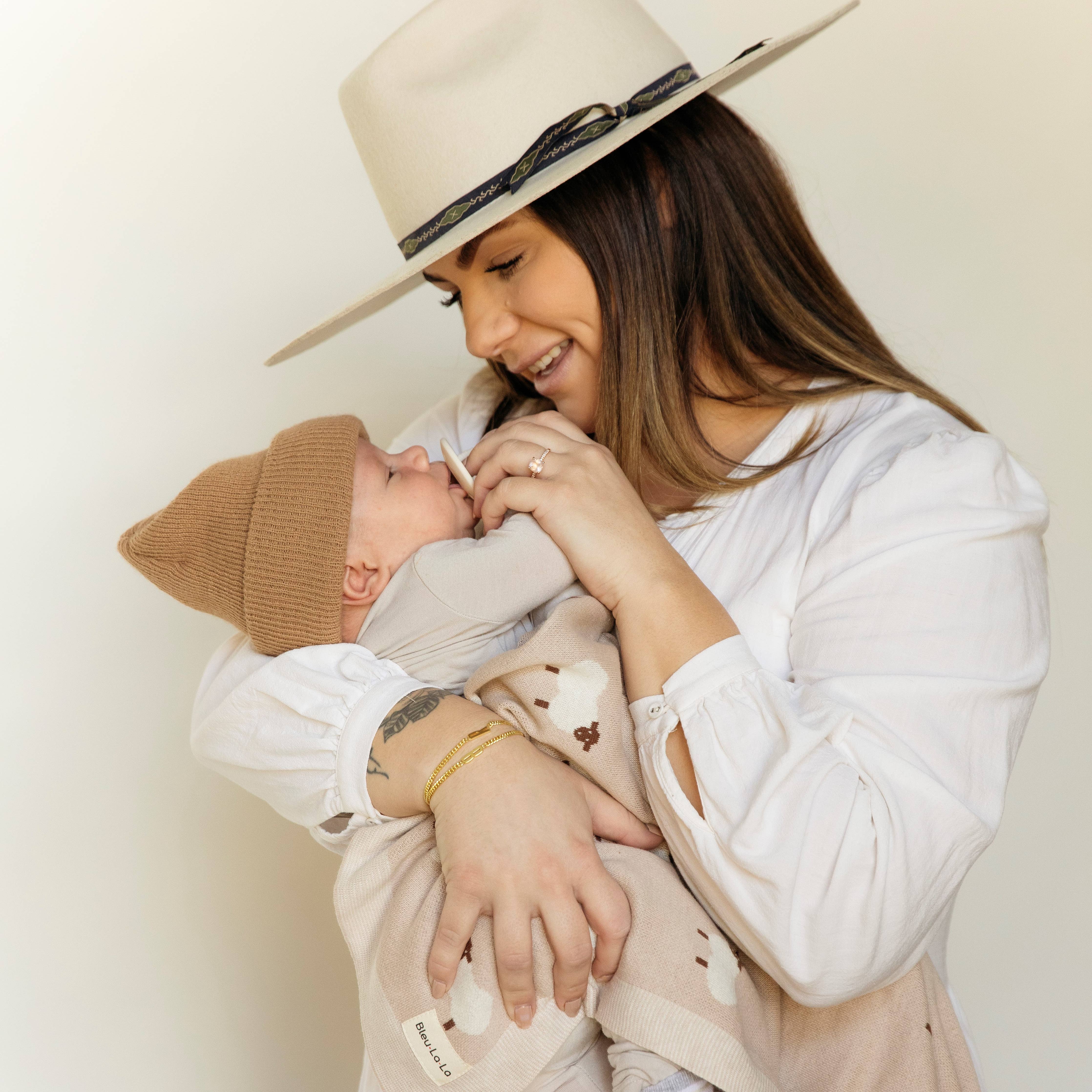 Woman wearing a beige hat holding a baby against a plain background