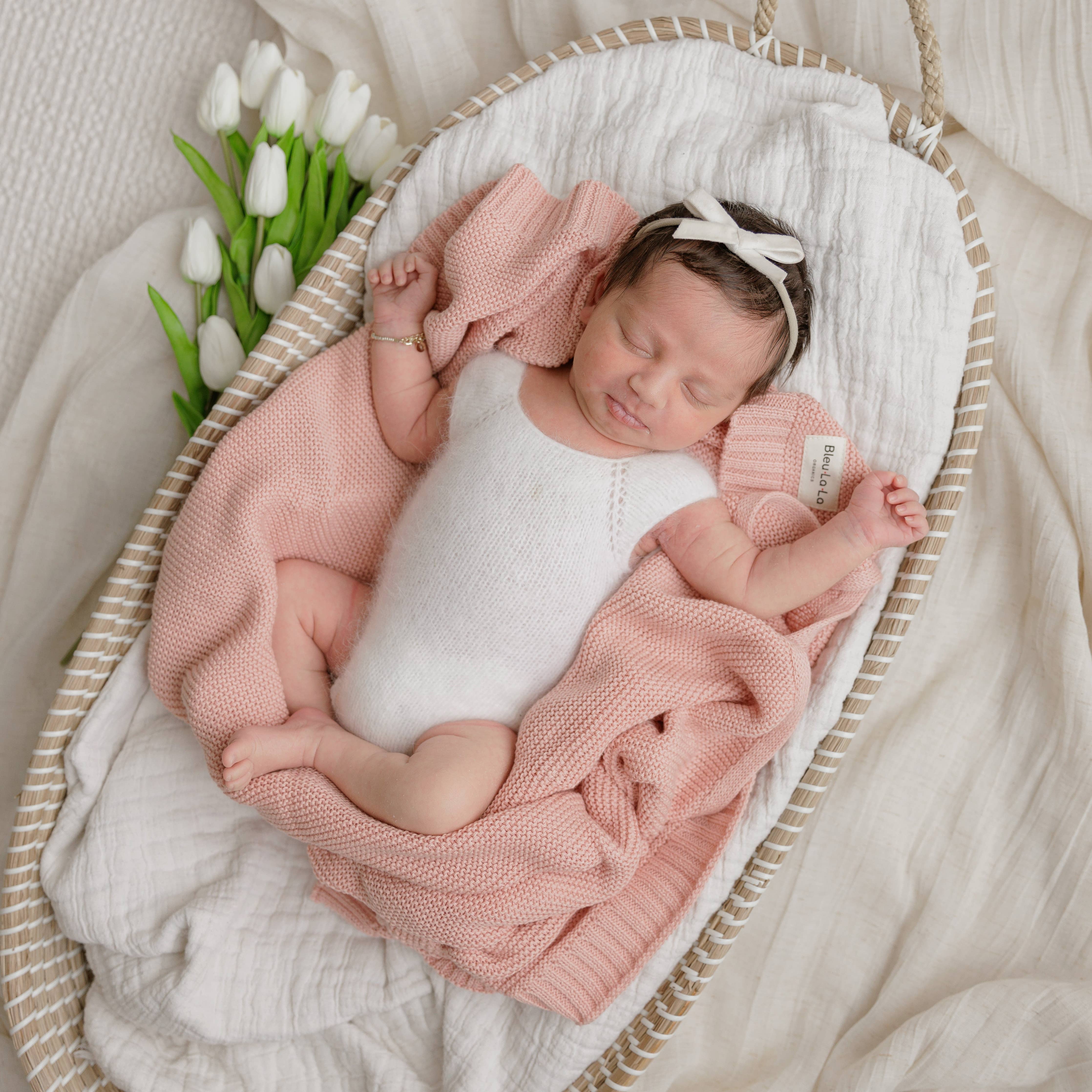 Newborn baby wrapped in pink blanket with white tulips in the background