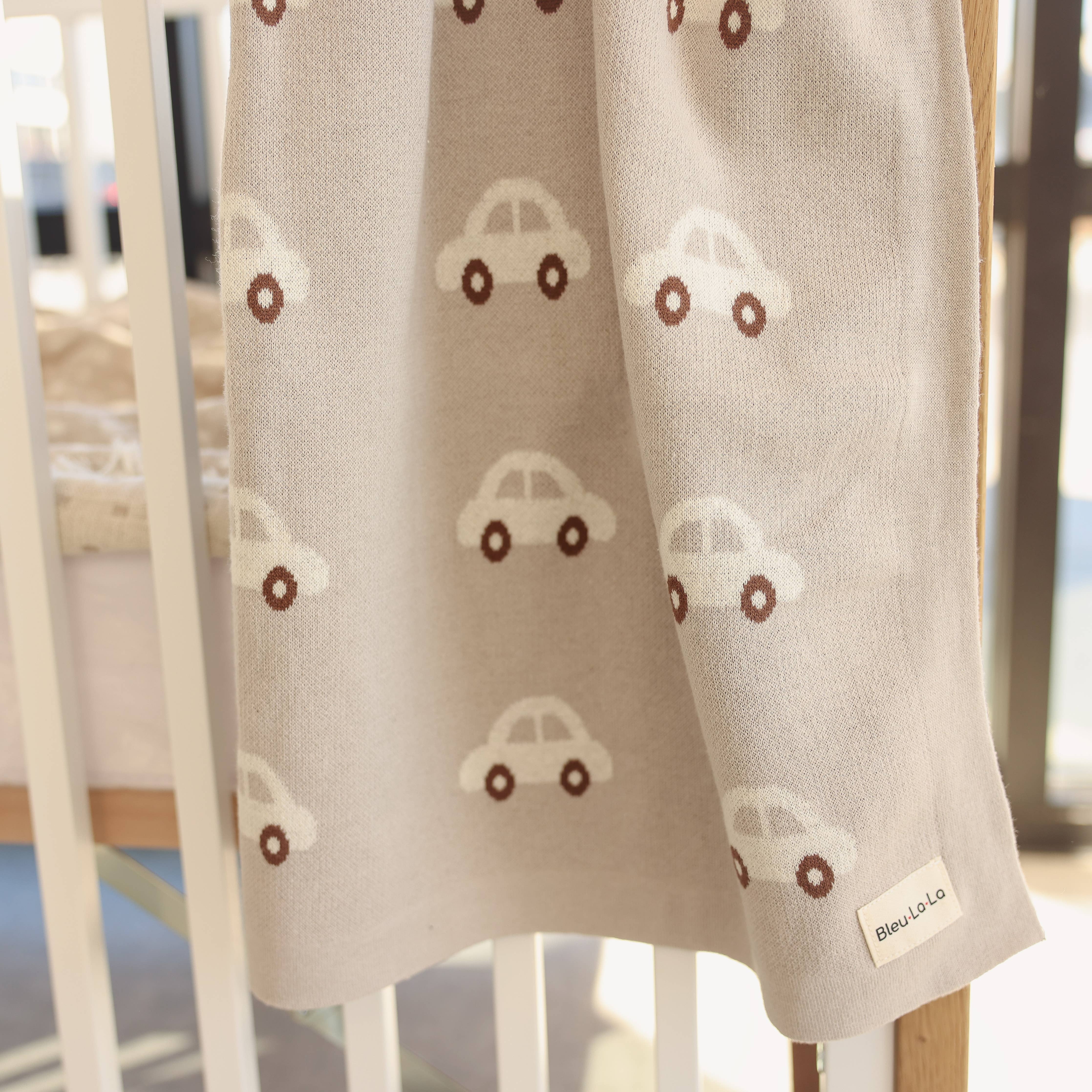 Baby blanket with car pattern draped over a crib