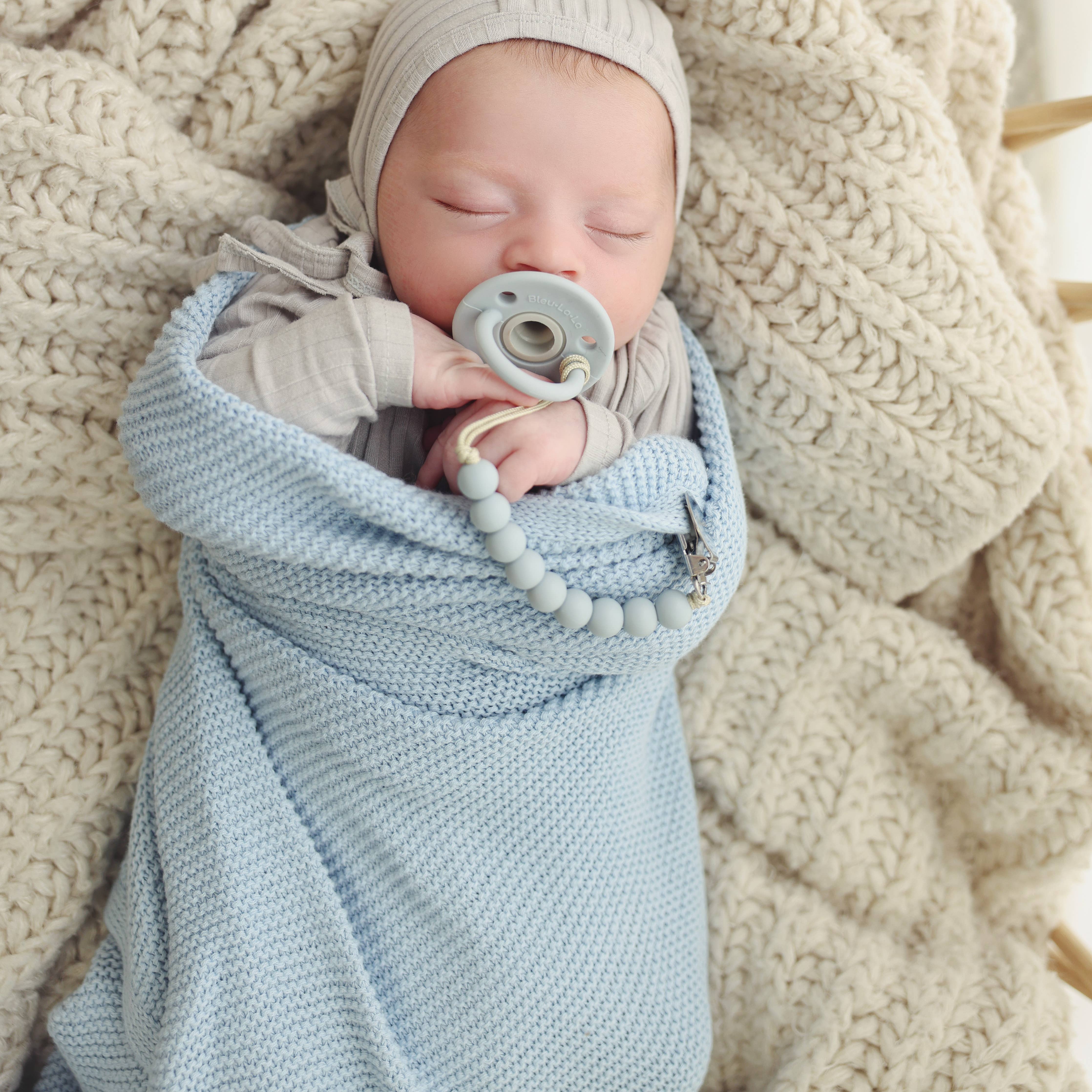 Newborn baby wrapped in a blue blanket with a pacifier, lying on a textured beige surface.