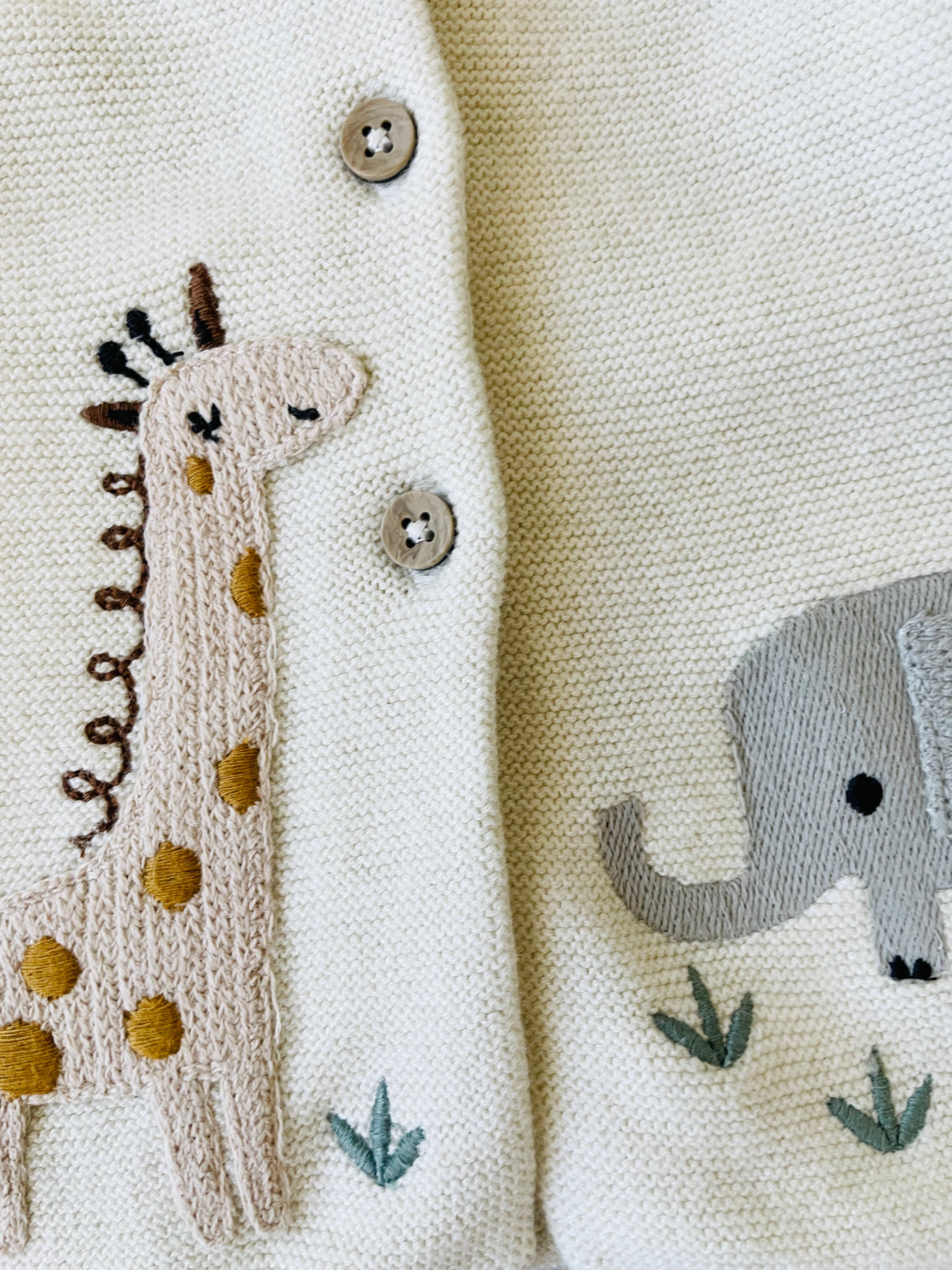 Close-up of a baby cardigan with embroidered giraffe and elephant designs.