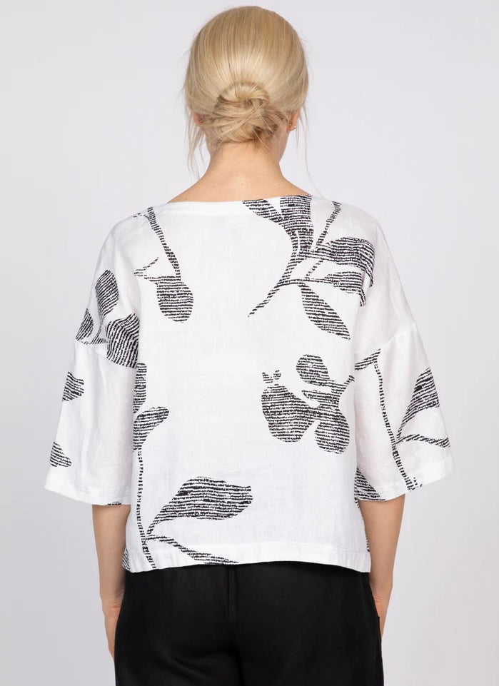 IMG_0128 (front, outdoor, dark-haired model): Woman wearing white linen Tessa top with bold black abstract floral print, v-neck and dropped shoulders, styled with printed wide-leg pants, outdoor setting
IMG_0129 (front, studio, blonde model): Front view of white linen Tessa top with oversized black abstract floral print and v-neckline, styled with black wide-leg pants on neutral background
IMG_0132 (full-length, outdoor, dark-haired model): Full-length front view of white linen Tessa top with bold black flo