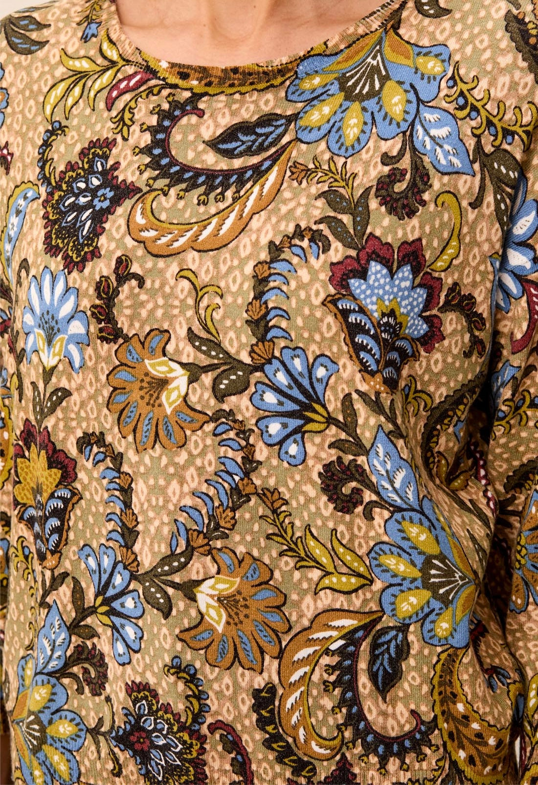 Close-up of a beige blouse with a detailed multicolor floral and paisley print in blue, yellow, brown, and red.