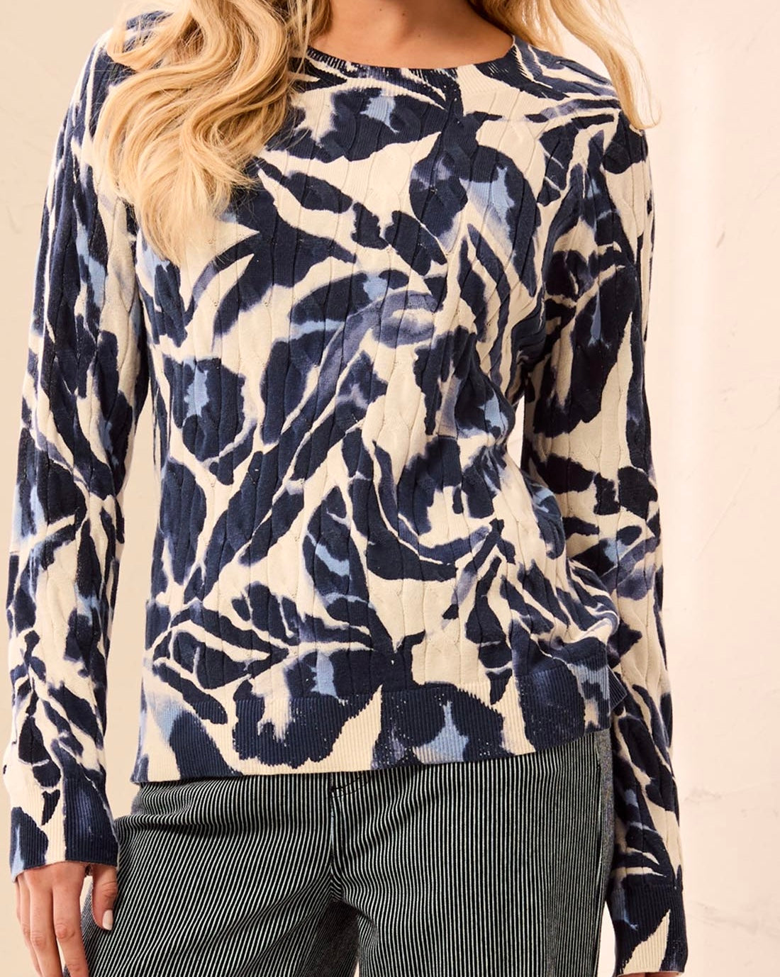 A woman wearing a long-sleeve top with a navy blue and cream abstract floral pattern, paired with dark pinstriped pants.