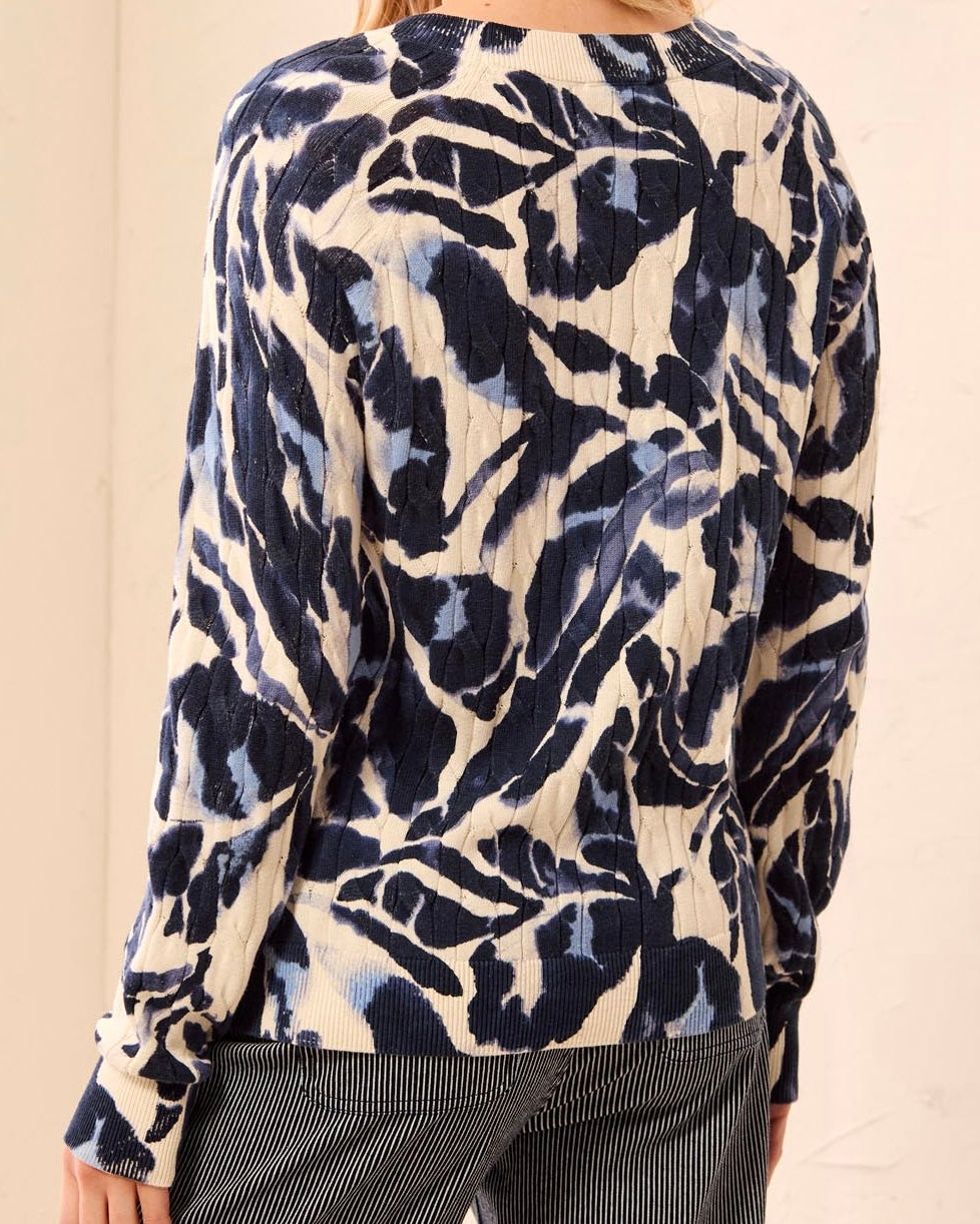 A woman wearing a long-sleeve textured top with a navy blue and cream abstract pattern, paired with dark pinstriped pants, shown from a rear three-quarter view.