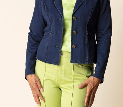 A cropped navy blue denim jacket with brown buttons, worn by a model over a lime green top and matching lime green pants, against a solid beige background.