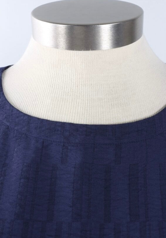 Close-up of a navy blue textured top on a cream ribbed mannequin neck with a brushed silver collar cap.