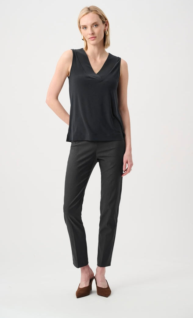 A woman modeling a black sleeveless V-neck top and black cropped trousers with brown heels, standing against a light gray studio background.
