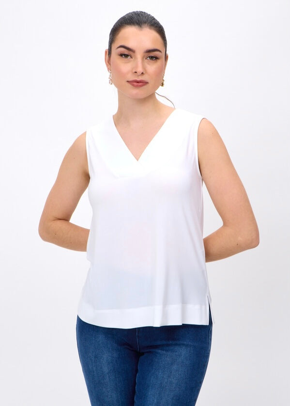 A woman modeling a sleeveless white V-neck top with blue jeans against a plain white studio background.