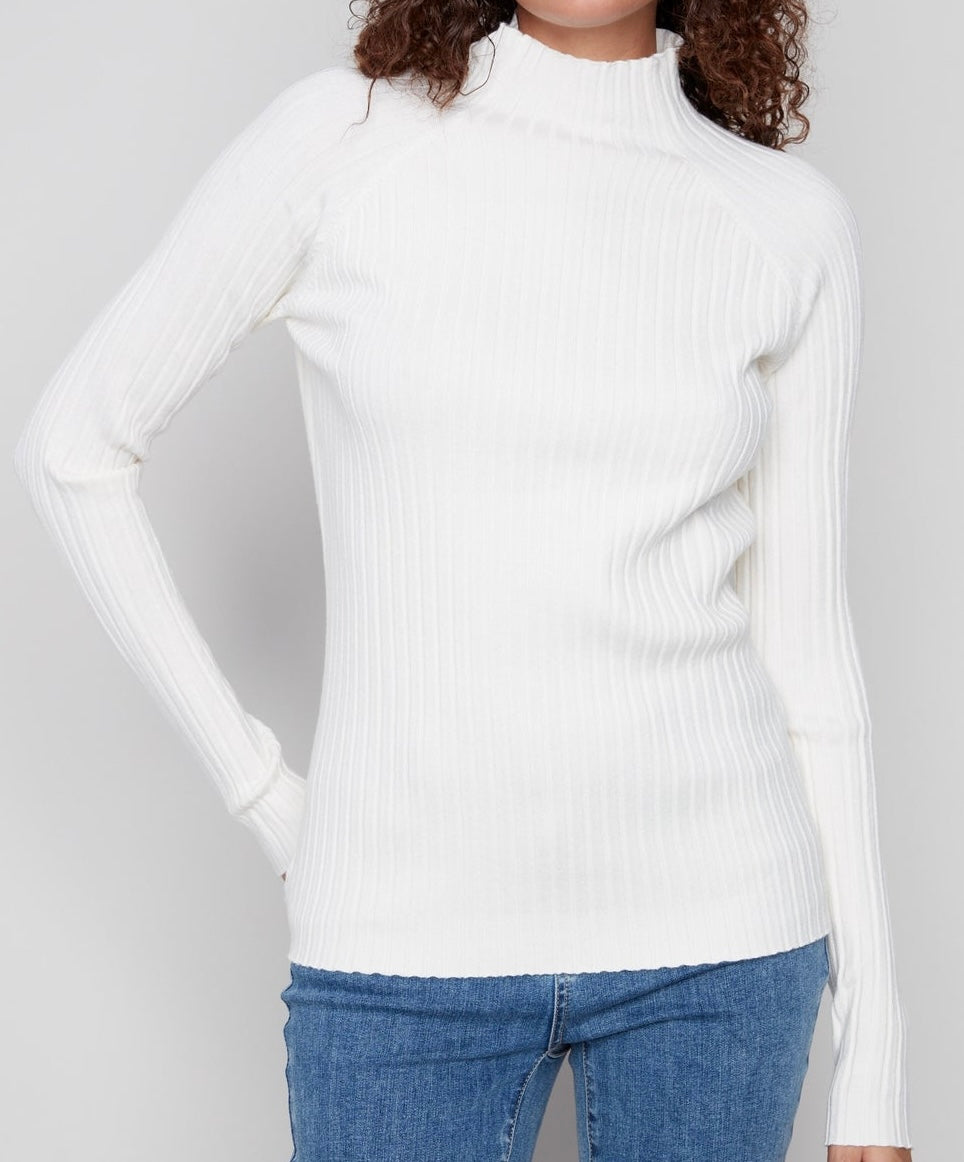 A woman wearing a white ribbed mock neck long-sleeve sweater and blue jeans, shown from the neck down against a light gray background.